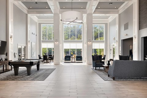 A large, open-concept living room with a pool table and a view of the trees outside the windows.
