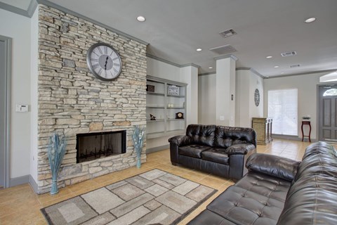 A living room with a stone fireplace and a black leather couch.