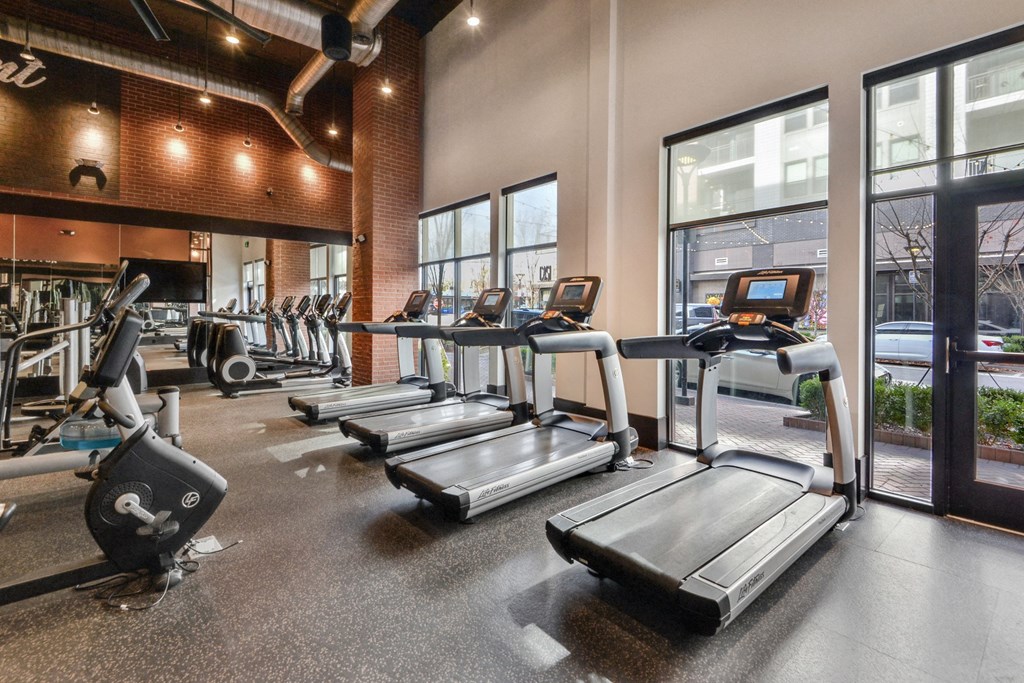 a gym with treadmills and other exercise equipment in a building with large windows