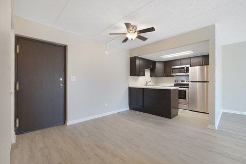 an empty living room with a kitchen and a ceiling fan