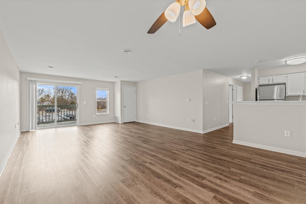 an empty living room with a ceiling fan and a kitchen