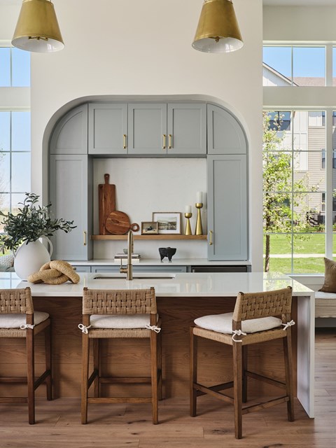 A kitchen with a white counter top and wooden chairs.
