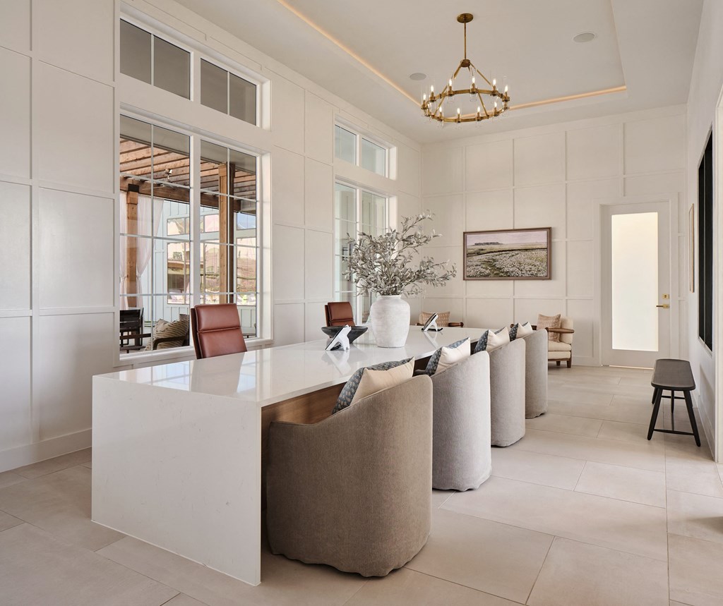 A white reception desk with a gold top is surrounded by beige chairs in a spacious room.