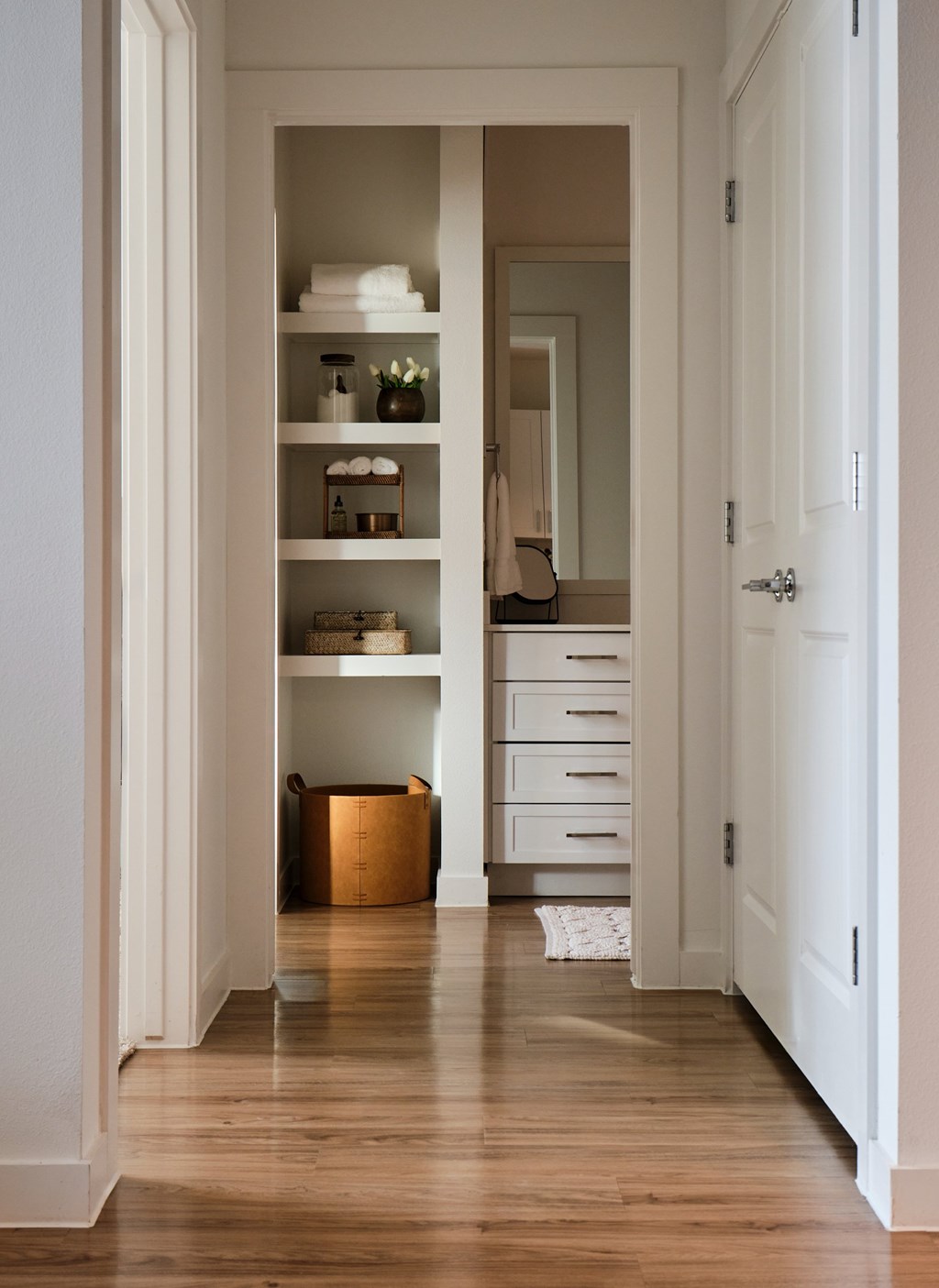 A hallway with a white door and a white cabinet with shelves.