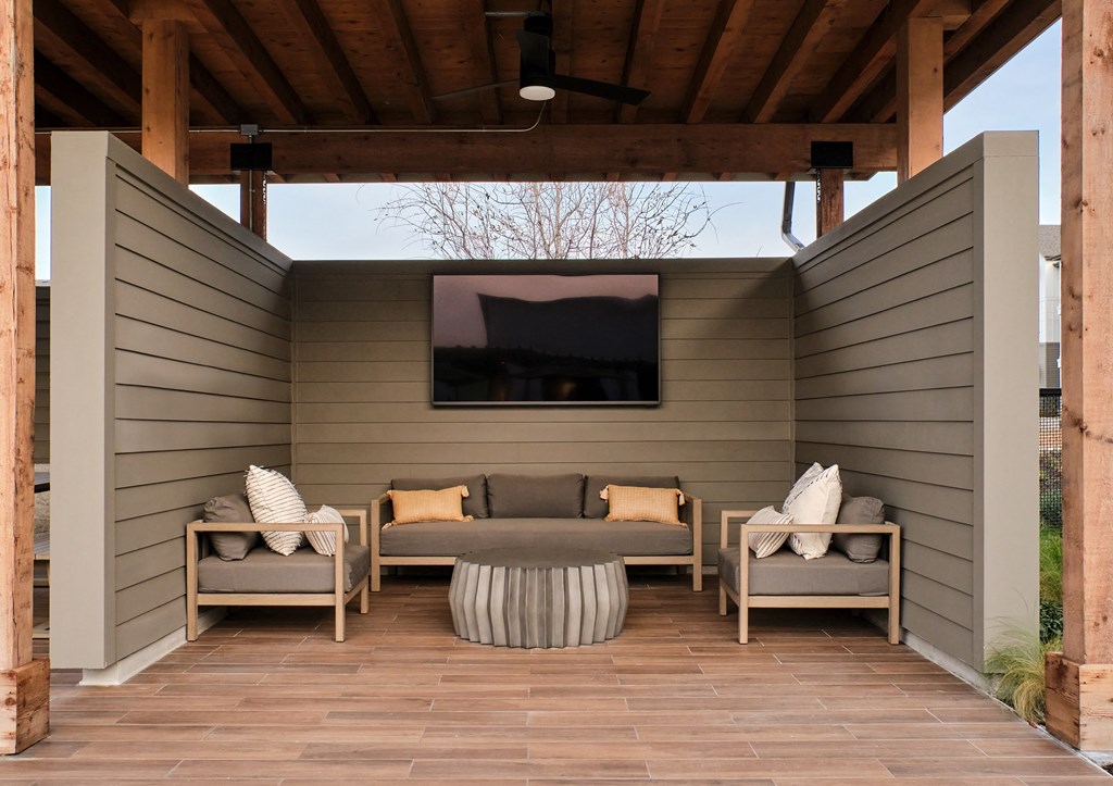 A wooden patio with a couch, chairs, and a TV.