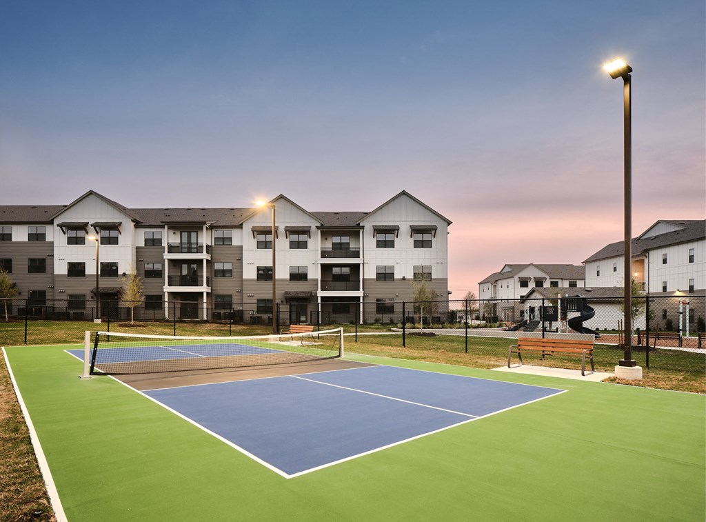 A tennis court is surrounded by apartment buildings.