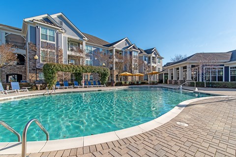 A large swimming pool in front of a building with a patio area.