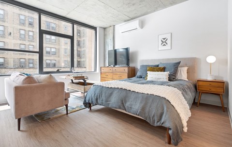 A bedroom with a large bed, a chair, and a window overlooking a building.