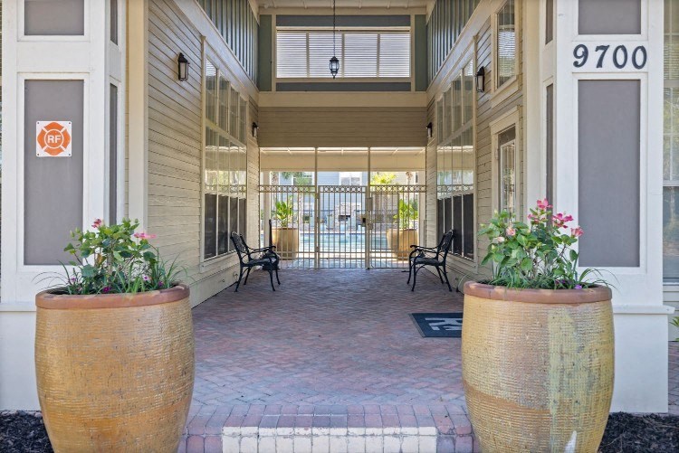 the front porch of an apartment building with chairs and plants