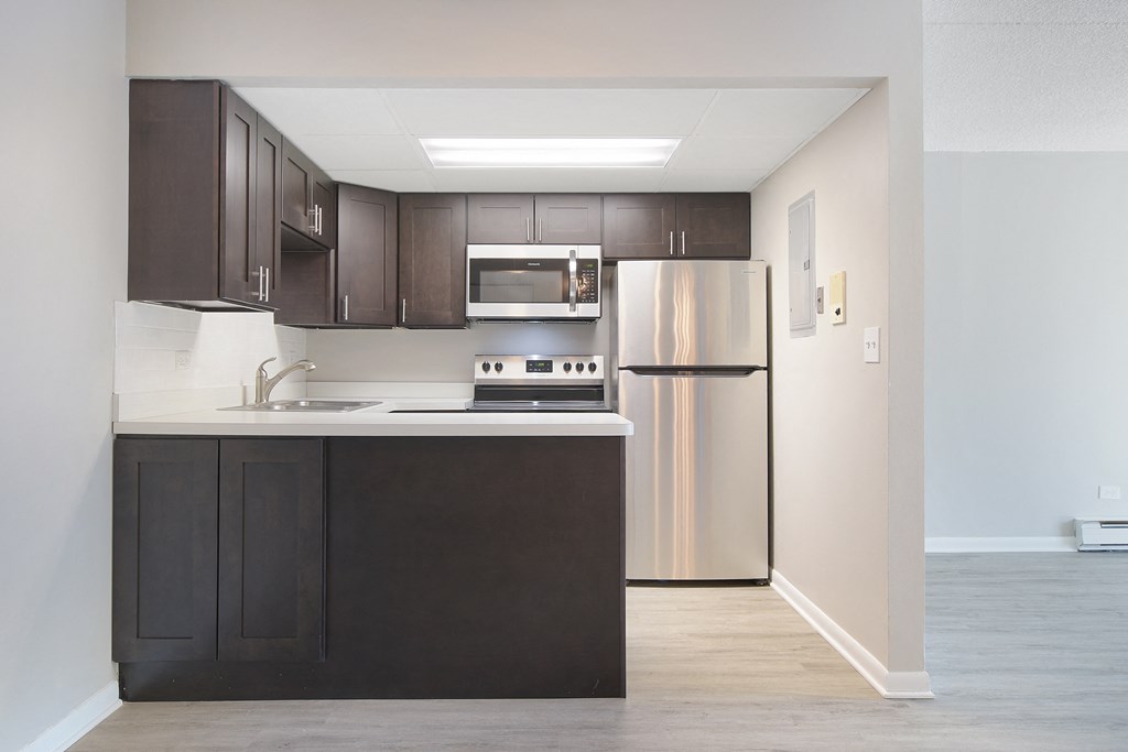 an empty kitchen with stainless steel appliances and dark wood cabinets