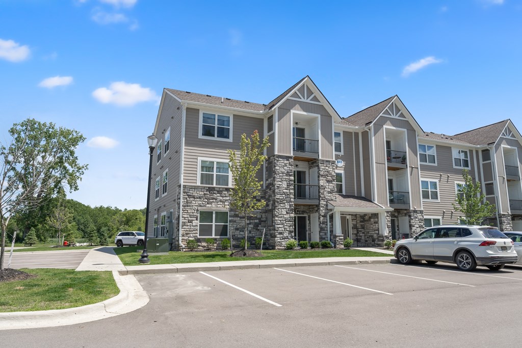 A silver car is parked in a parking lot in front of a large apartment building.