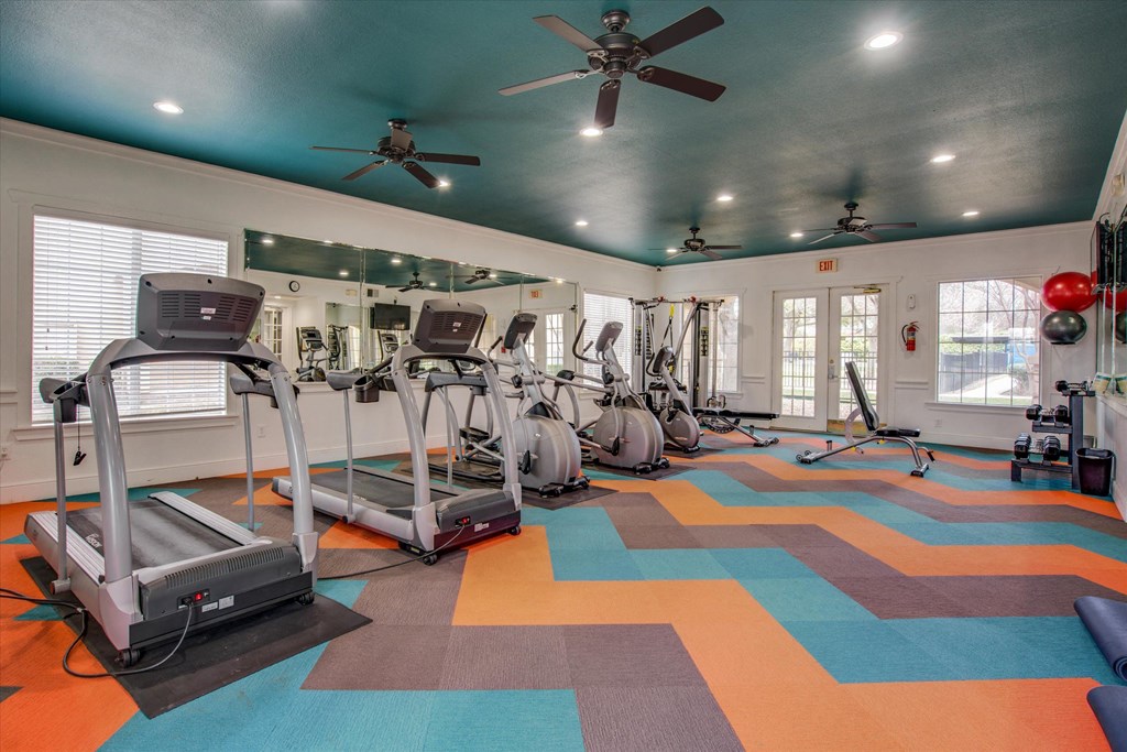 a gym with weights and cardio equipment on the floor and a ceiling fan