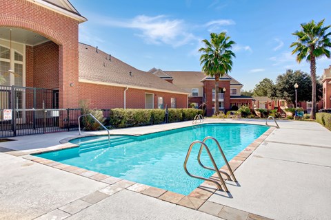 A swimming pool in front of a brick building with palm trees in the background.
