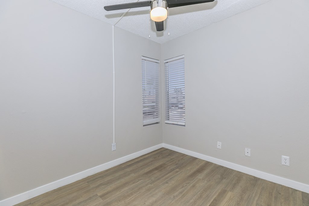 an empty bedroom with a ceiling fan and two windows
