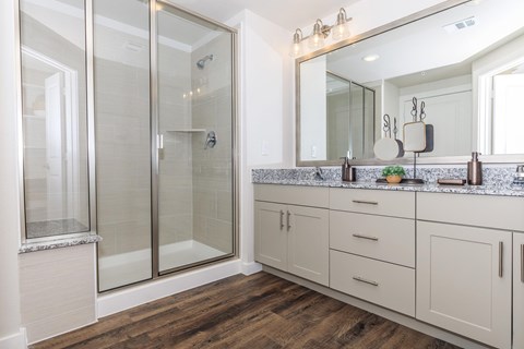 A bathroom with a walk-in shower, a vanity with a mirror, and wooden floors.
