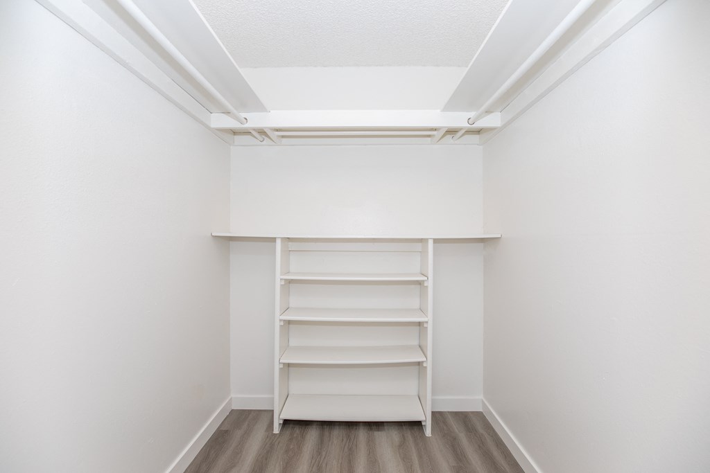 a small walk in closet with white walls and wooden shelves