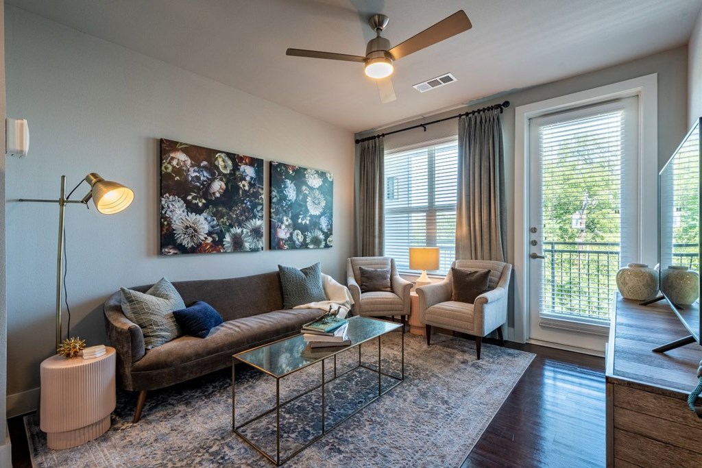 A living room with a brown couch, a glass coffee table, and a ceiling fan.