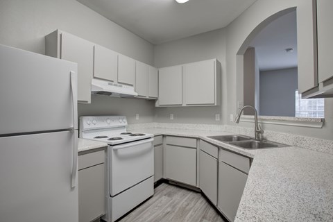 A white kitchen with a refrigerator, stove, and sink.
