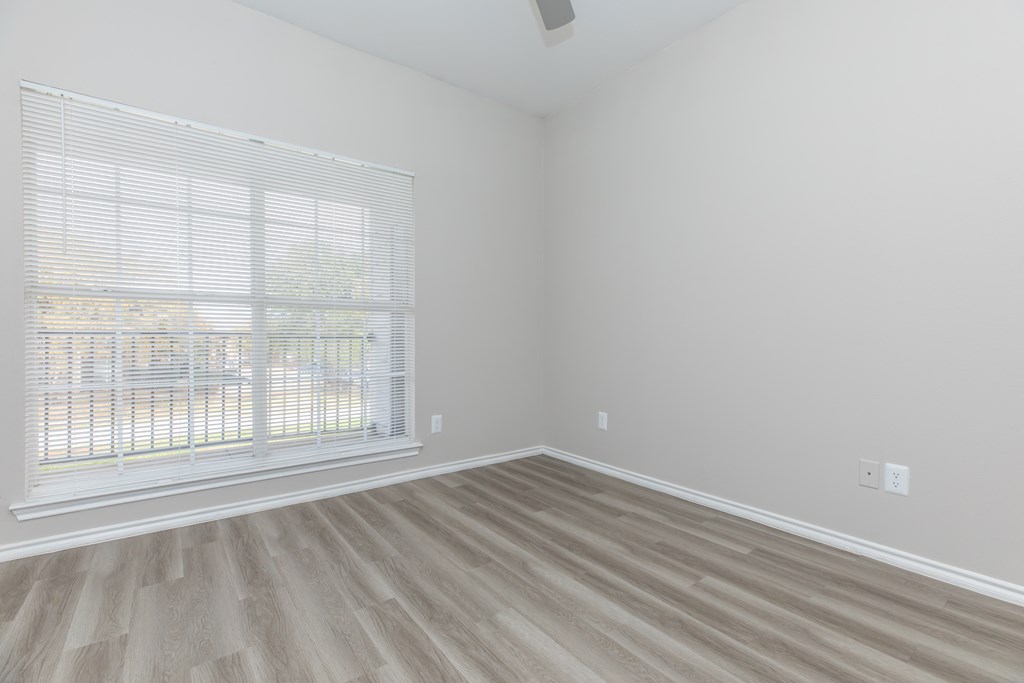 an empty bedroom with a large window and hardwood floors