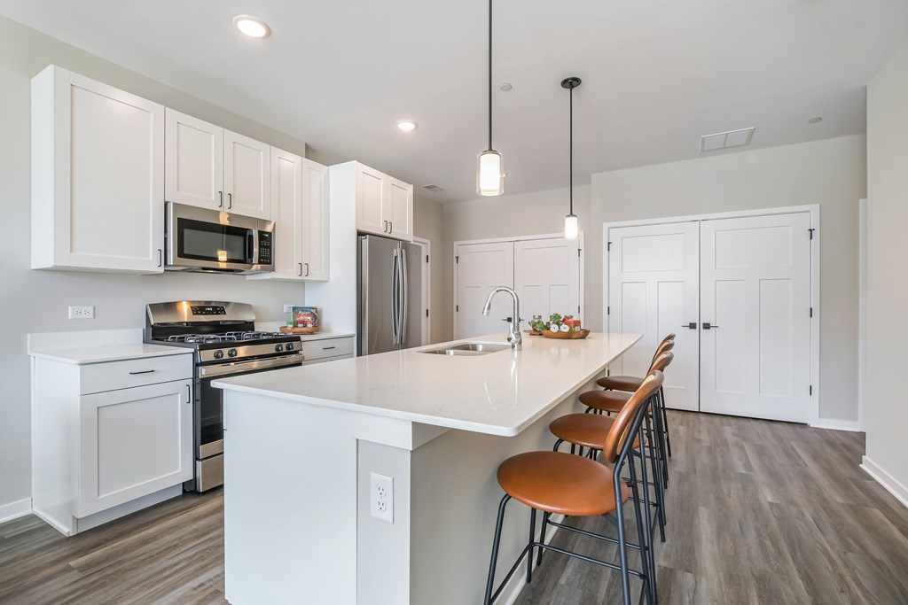 A kitchen with white cabinets and a white island with brown chairs.