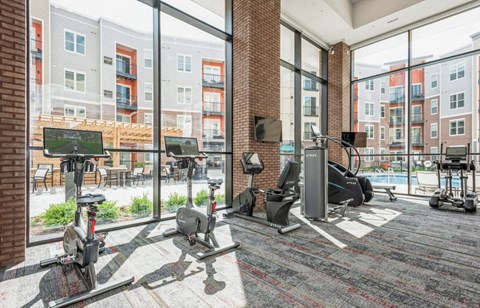 A gym with a brick wall and a view of apartment buildings outside the windows.