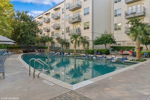 A large swimming pool in front of a building with a poolside lounge.