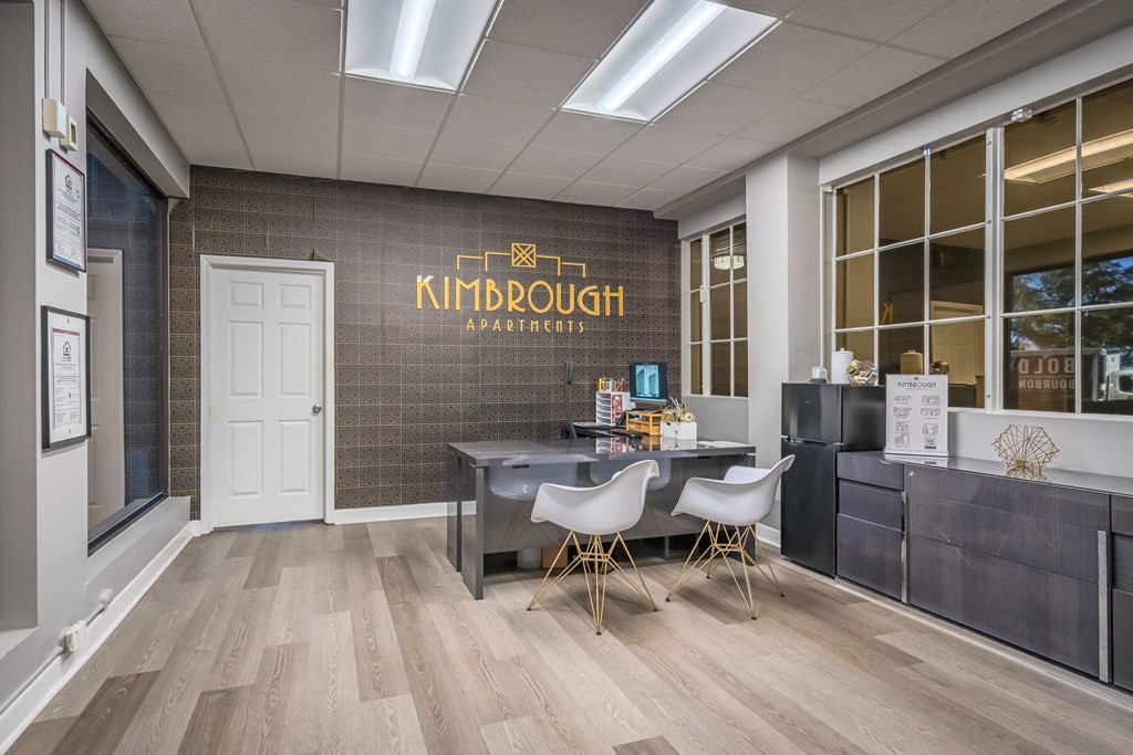a reception area with a desk and chairs in front of a wall with a logo