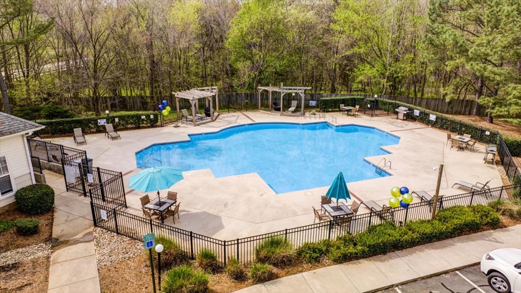 a swimming pool with chairs and umbrellas in a backyard with trees