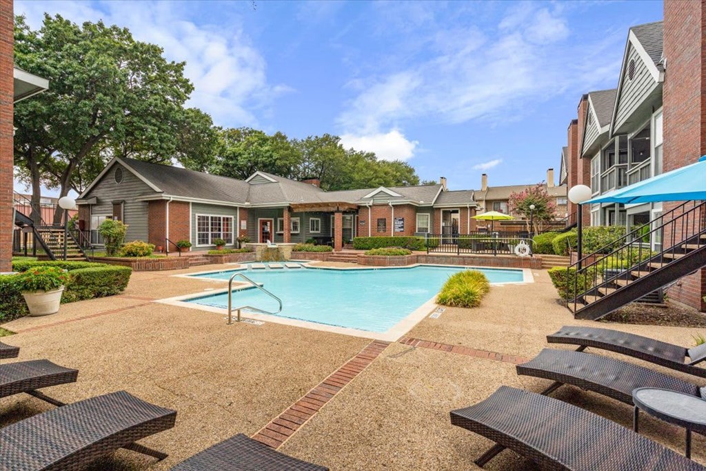 A pool surrounded by picnic tables and a brick building in the background.