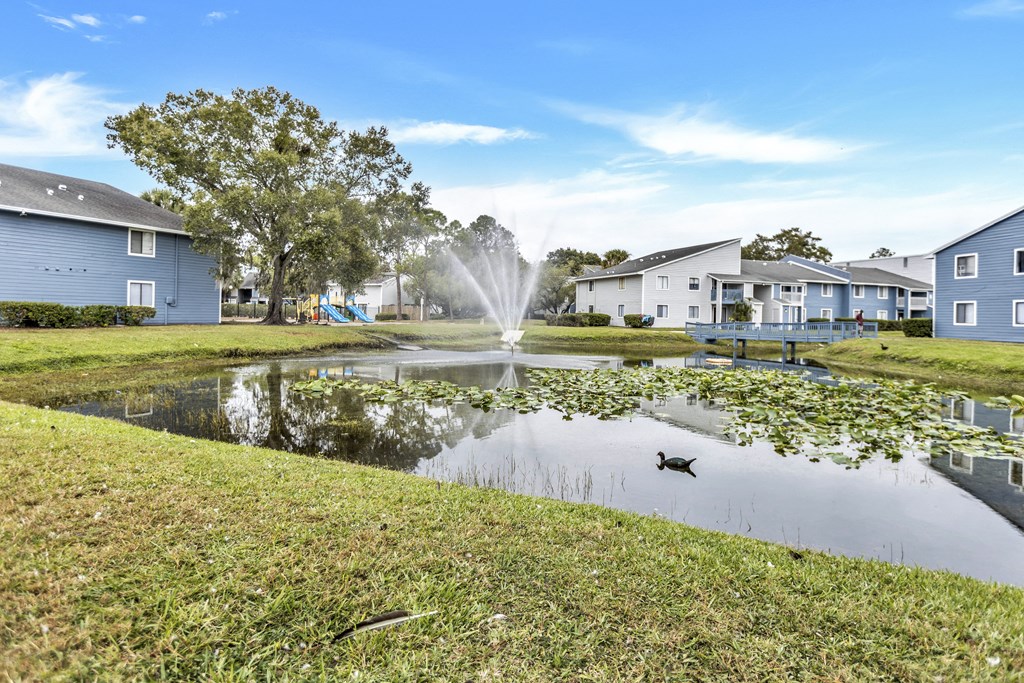 a pond with a fountain in the middle of some houses