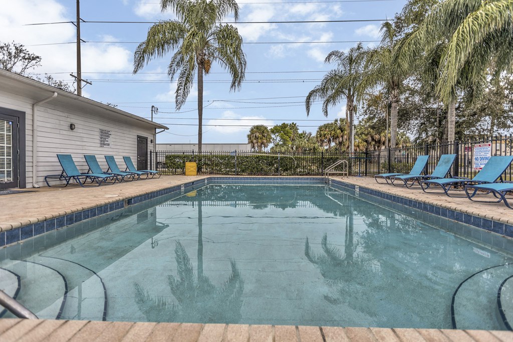 a pool with blue chairs and palm trees next to a house