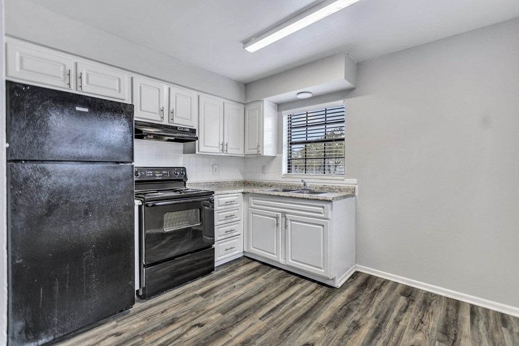 an empty kitchen with white cabinets and a black refrigerator