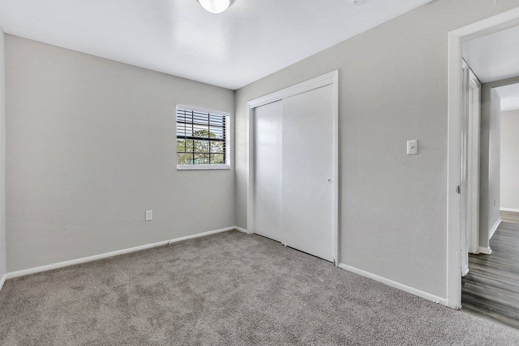 a bedroom with white walls and carpet and a door to a closet