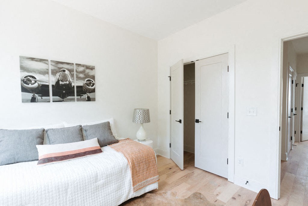 a bedroom with white walls and a bed with grey and orange pillows