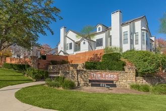 a stone retaining wall with a sign that says the tides in front of a large white house