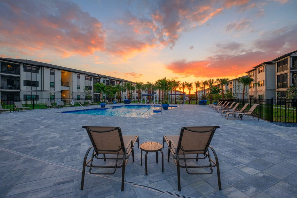 an outdoor patio area with chairs and a pool at sunset