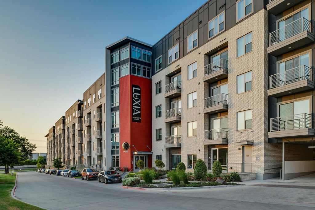 A street view of a row of apartment buildings with cars parked on the side.