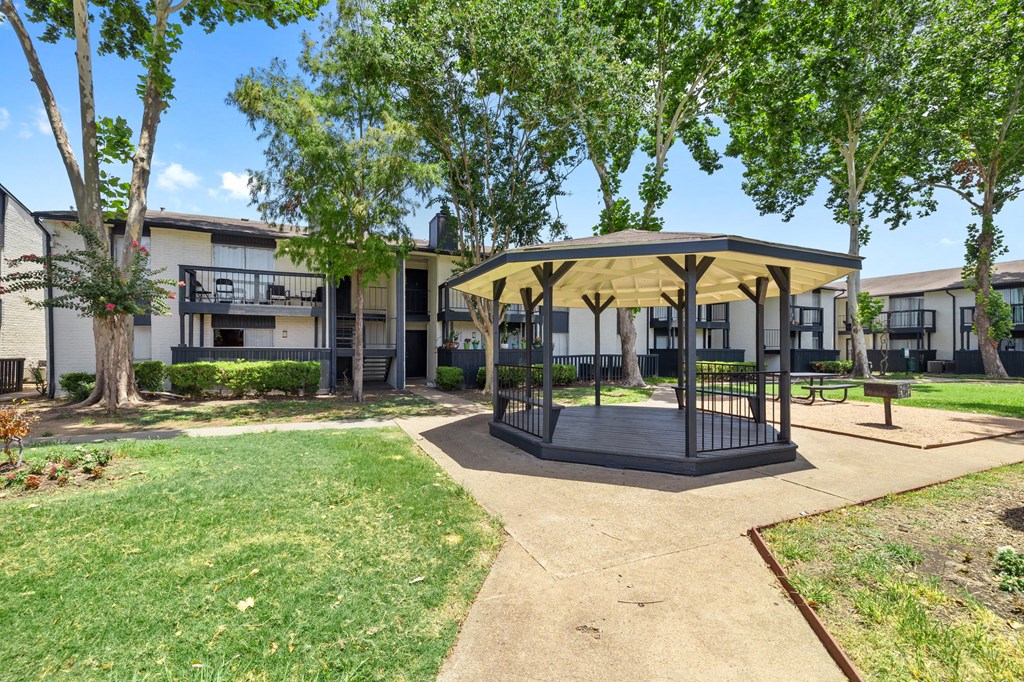 a gazebo with trees and apartments in the background
