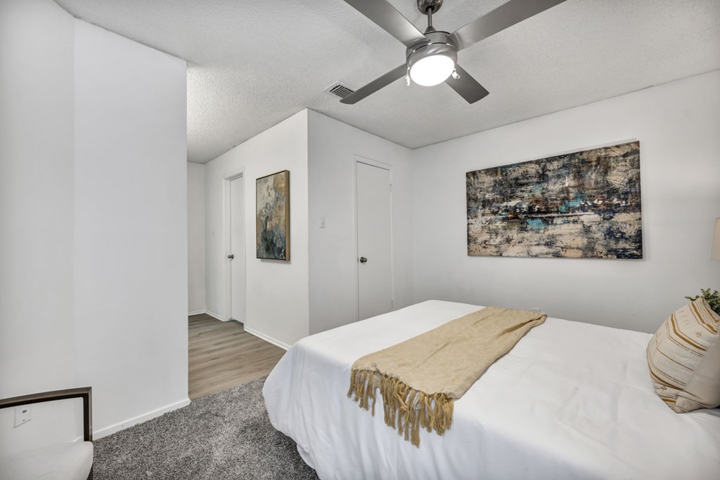 A bedroom with a bed, a ceiling fan, and a painting on the wall.