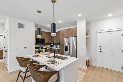 A modern kitchen with a white island and brown chairs.