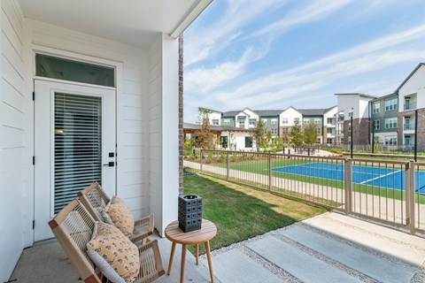 A patio with a chair and table overlooking a pool.