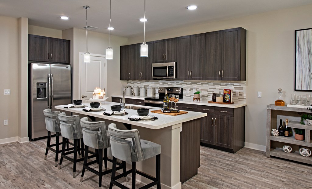 a kitchen with a large island with bar stools and a stainless steel refrigerator