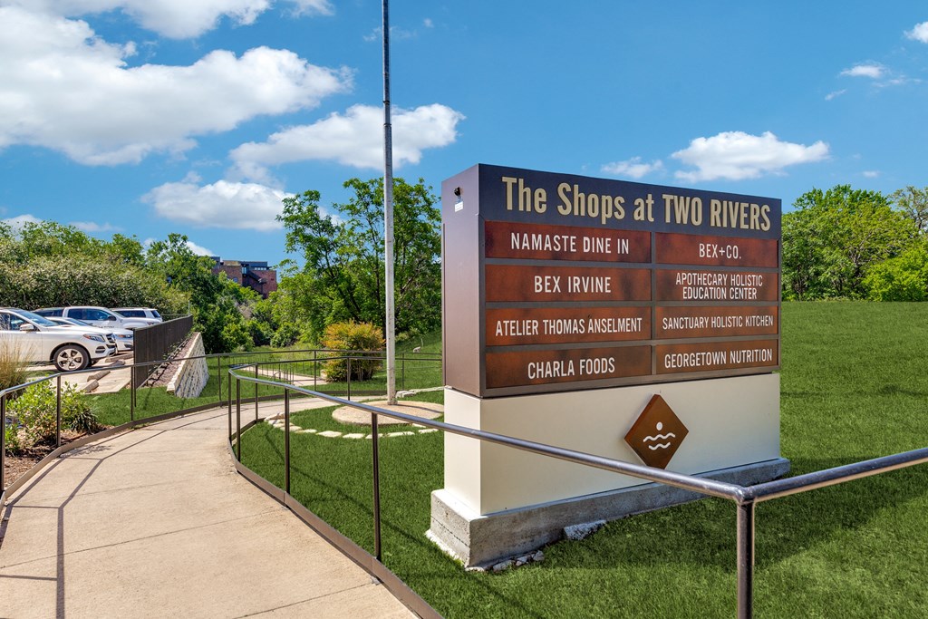 a sign for the shops at two rivers at the entrance to a park with cars