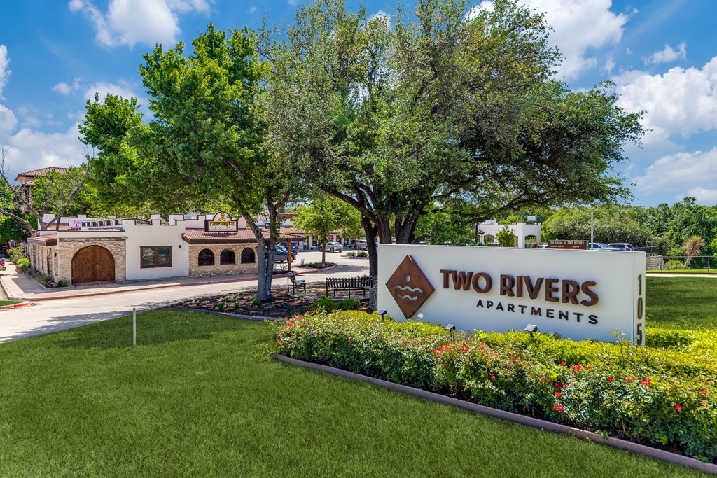 a sign for two rivers apartments in front of a garden and trees