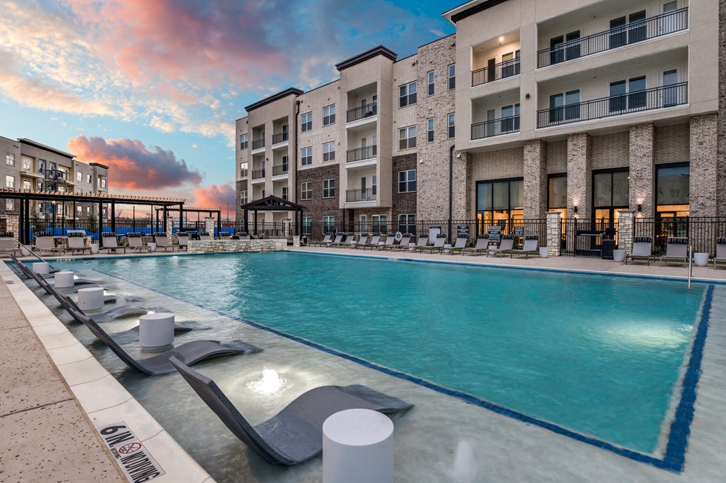 a swimming pool with an apartment building and a sunset in the background
