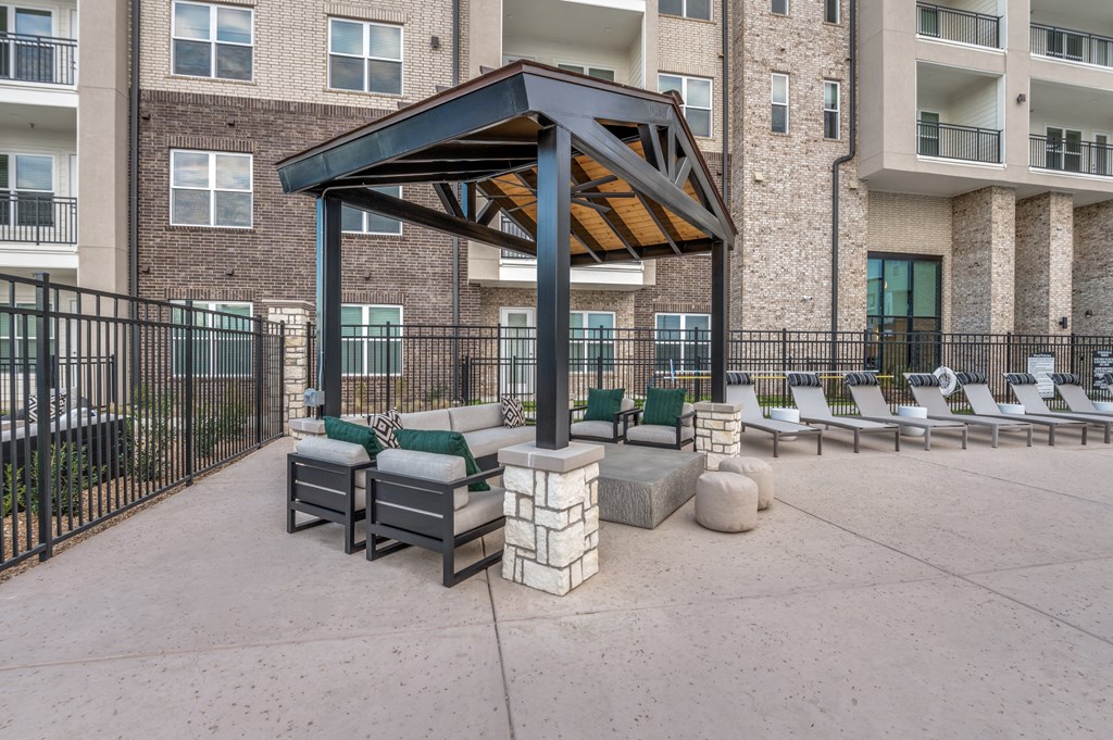 an outdoor patio with lounge chairs and a pavilion in front of an apartment building