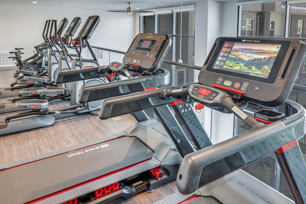 a gym with several treadmills and a monitor on a table