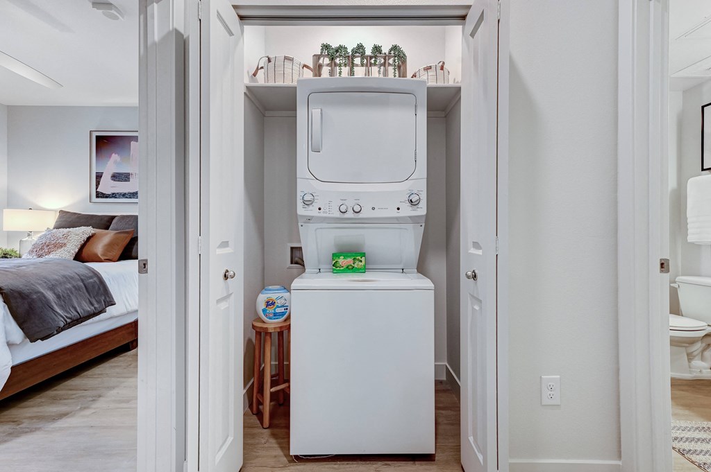 a white washer and dryer in a white laundry room with a bed