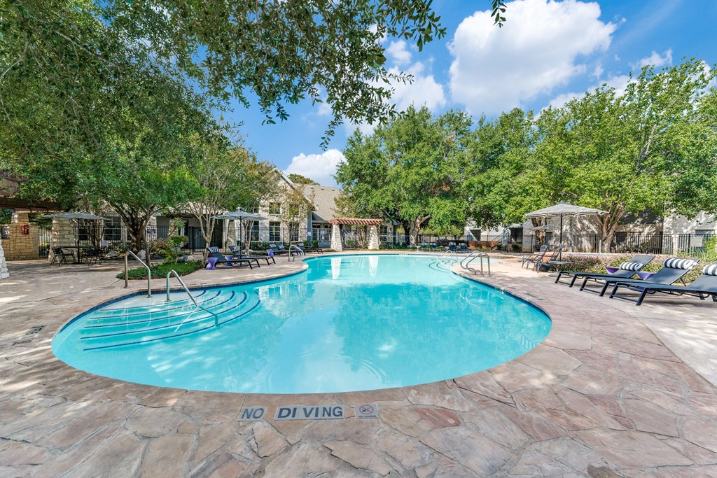 a resort style swimming pool with chairs around it and trees