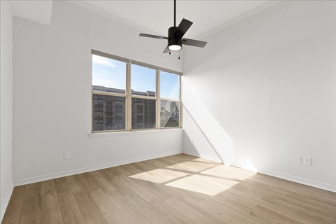 A room with a ceiling fan and a window overlooking a building.